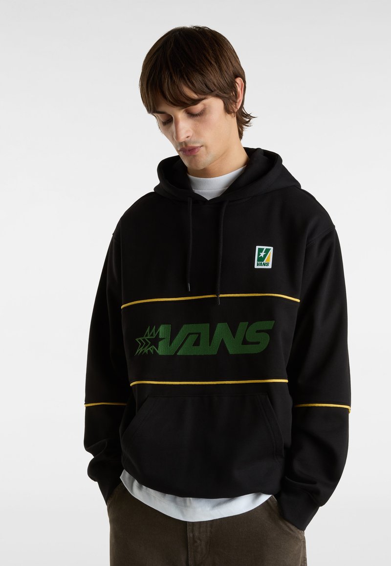 Svart huvtröja med grön "VANS"-logga, gula stripes detaljer och en framficka. Har ett mysigt tyg och justerbar dragsko på huven.