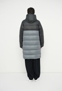Pametna puffer jakna s kapuljačom, u crno-sivoj kombinaciji boja. Meki materijal, odvojiva kapuljača i duži kroj koji doseže do sredine bedara.