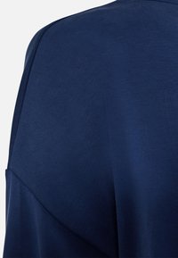 Tessuto blu navy con una trama liscia, caratterizzato da una vestibilità ampia e una caduta sottile. I dettagli delle cuciture sono visibili nella zona delle spalle.