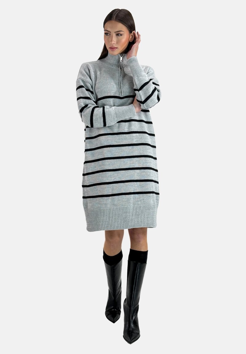 Robe en maille de couleur gris clair avec des rayures horizontales noires, col haut avec une fermeture éclaire, poignets et ourlet côtelés, portée avec des bottes noires allant jusqu'aux genoux.