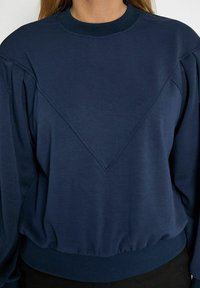 Navy blue sweatshirt made from soft material, featuring a textured triangular design on the front, ribbed neckline, and elastic waistband.