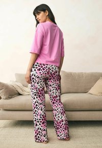 Roze top met korte mouwen gecombineerd met wijd uitlopende broek met een roze en zwarte luipaardprint op een witte achtergrond. Vlakke textuur, casual ontwerp.
