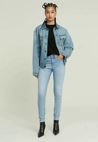 Džínová bunda v světle modré barvě, volný střih s knoflíky, kombinovaná s černým topem a světle modrými skinny džíny. Nosené s černými kotníkovými botami na podpatku.