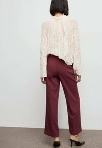 Blusa ligera y texturizada con espalda drapeada y detalle de cuello atado, combinada con pantalones anchos de un burdeos intenso y mules oscuros de tacón.