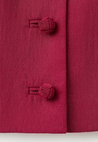 Deux boutons noués en tissu rouge fixés sur un tissu rouge tissé assorti avec des boutonnières visibles sur un vêtement.