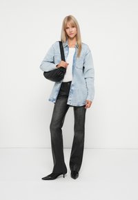 Světle modrá džínová oversize košile, bílý tričko, černé zvonové džíny, černá kabelka, špičaté černé boty, hladká textura po celém oblečení.