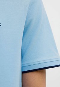 Polo shirt azzurro chiaro con tessuto a trama, maniche corte e un accento blu navy lungo l'orlo delle maniche.