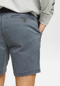 Mørkegrå shorts lavet af en blanding af bomuldsstof, med en baglomme med knaplukning og opbagt kant.