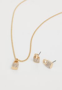 Gouden ketting met een slotvormige hanger en bijpassende oorbellen, gekenmerkt door een gestructureerd oppervlak en versierd met heldere sprankelende stenen.