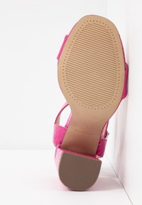Sandale à talon haut rose avec dessus en cuir texturé, bride de cheville réglable et semelle en caoutchouc rainurée avec dessous beige clair.