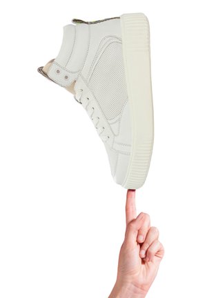 Sneaker alta bianca con pannelli perforati, suola piatta e accenti colorati sulla linguetta, tenuta in verticale su una punta.