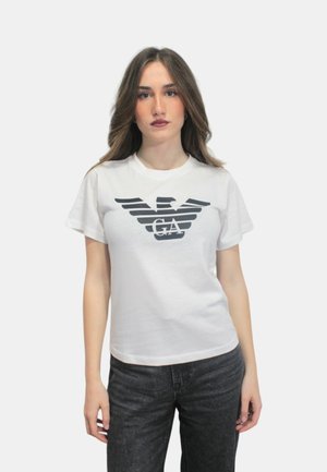 Hvid bomulds t-shirt med korte ærmer, der har et sort ørnegrafik og teksten "GA" centreret under designet. Enkel, afslappet pasform.