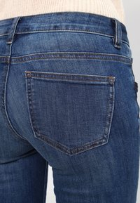 Jeans de mezclilla de un azul oscuro con un diseño ajustado. Incluyen costuras visibles, un bolsillo trasero y una textura suave.