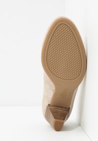Chaussure à talon haut beige avec une tige lisse et une semelle en caoutchouc texturée. Présente une silhouette étroite et une finition subtilement brillante.