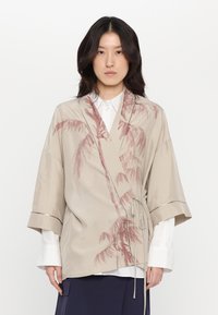 Beige spalvotu kimono stiliaus švarkas su dulkių rožinės spalvos palmės lapų printu. Plačios rankovės ir surišamas užsegimas. Subtilūs metaliniai akcentai.