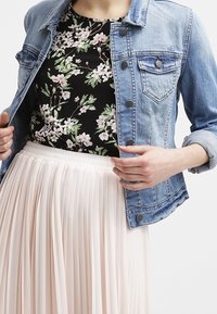 Jeansjacka med metalldetaljer, svart blommig topp och veckad ljusrosa kjol. Har en strukturerad design med avslappnad passform.