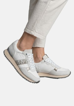 White and gray sneakers with laces worn with light beige pants, showing side and top view of both feet on a plain background.