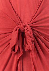 Rostfarget stoff med en knyttede detalj i sentrum, som har draperte folder og en myk, teksturert overflate.
