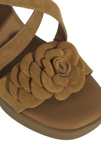 Brown suede sandal featuring a large layered flower design on the upper, with crisscross straps and a smooth, rounded sole.