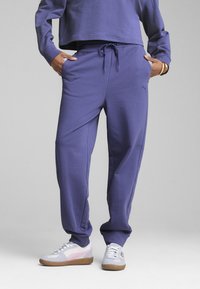 Lilla sweats bukser lavet af blødt materiale med elastisk talje og sidelommer, parret med lyse sneakers med pink detaljer.