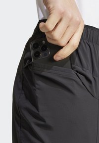 Czarne szorty z miękkiego, teksturowanego materiału, z boczną kieszenią, do której wkładany jest smartfon. Widoczny elastyczny pas.