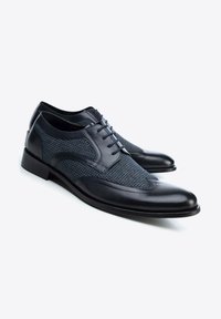 Zapatos oscuros de cordones en azul marino, con parte superior de tejido texturizado que presenta un patrón a cuadros y acentos de cuero suave en la puntera y los lados.