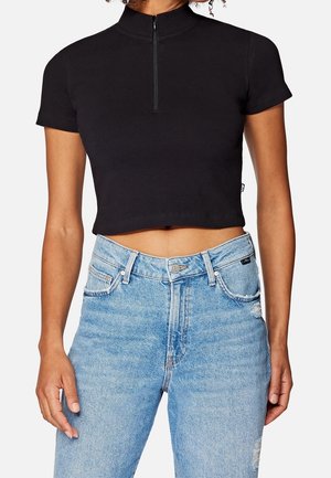 Sort kortærmet top med lynlås i kraven, parret med højtaljede lyseblå slidte jeans.