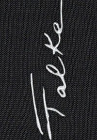 Cuciture bianche in corsivo che formano la parola "fretex" su uno sfondo di tessuto lavorato a maglia nero.