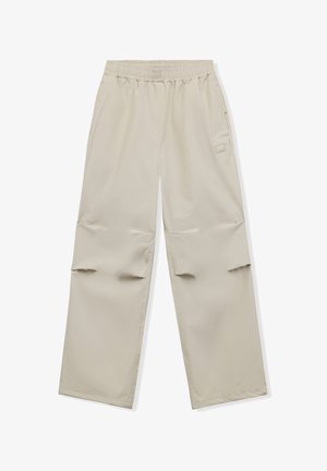 Pantalones beige de pierna ancha con cintura elástica y bolsillo lateral, con un pequeño parche rectangular en la parte superior del muslo.