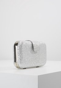 Pochette argentée couverte de petits rhinestones, de forme rectangulaire, avec des accoutrements en métal et une fermeture à pression. Texture lisse.