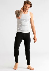 Pilkas be rankovių marškinėlis ir juodos tamprės stovinčiam vyrų modeliui. Marškinėliai pagaminti iš minkšto, medvilnės tipo audinio.