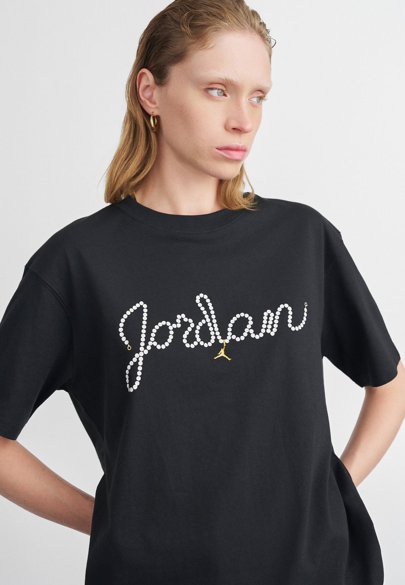 T-shirt in cotone nero con una grafica in strass bianchi che forma la scritta "Jordan" con un accento del logo Jumpman dorato. Maniche corte e vestibilità rilassata.