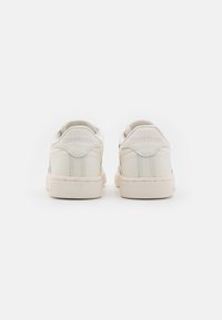 Bílé kožené tenisky s hladkým povrchem, se kontrastní béžovou gumovou podrážkou a jemným brandingem Reebok ve světle růžové na patě.