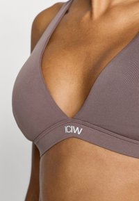 Σουτιέν σε απαλό καφέ χρώμα, με V-λαιμόκοψη, λεία υφή και λευκό λογότυπο στη βάση. Ρυθμιζόμενοι ιμάντες για καλή εφαρμογή.