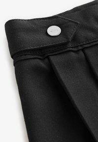 Sort stof med en tekstureret finish, der har et plisseret design og en sølvfarvet logo-knap med påskriften "Clarks" til lukning.