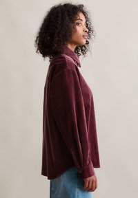 Bordeaux rode corduroy blouse met een gekragen hals, lange mouwen en met knopen afsluitbare manchetten. Zachte textuur, comfortabele pasvorm en een geribbelde structuur over het hele kledingstuk.