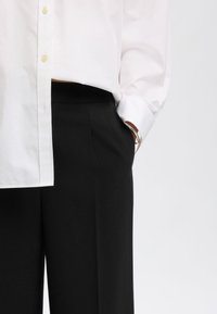 Witte knop-up shirt met lange mouwen, gecombineerd met hoge zwarte broeken, die een zachte textuur en een relaxte pasvorm laten zien.