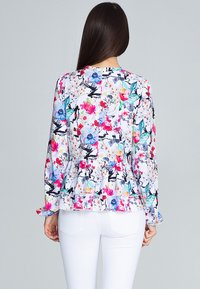 Bloemige blouse met lange mouwen en een peplum ontwerp, met levendige kleuren op een witte achtergrond en gerimpelde manchetten. Zachte stof met delicate patronen.