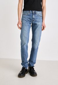 Lichtblauwe denim jeans met een rechte pasvorm, vijf zakken, subtiele vervaging en een knoopsluiting. Draagt met zwarte schoenen.
