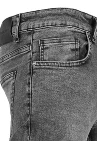 Vaqueros de mezclilla gris con una textura suave, que presentan un parche de cuero negro en la cinturilla y un diseño estándar de bolsillo trasero.