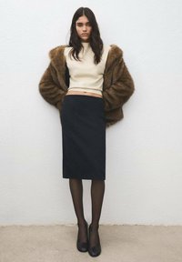 Stickad krämfärgad topp som slutar ovanför midjan, kombinerad med en tajt svart pennkjol, kompletterad med en brun fuskpälsjacka och svarta klackar.