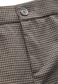 Brown and gray houndstooth patterned fabric with a smooth texture, featuring a metal button closure and stitched detailing at the waist.