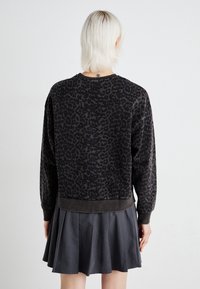 Sweat-shirt imprimé léopard noir et gris avec poignets et ourlet côtelés. Coupe ample avec un col rond, associé à une jupe plissée foncée.