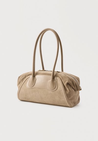 Τσάντα χειρός από μπεζ σουέτ και δέρμα με δύο μακριές λαβές και κλείσιμο με φερμουάρ, όρθια σε απλό φωτεινό φόντο.