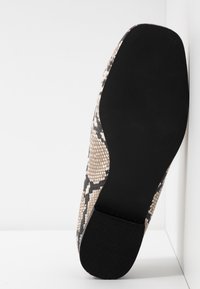 Chaussure à talon haut avec un motif serpent texturé beige et noir, dotée d'une semelle en caoutchouc noir lisse et d'un design à bout rond.
