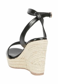 Sandalo wedge in pelle nera con cinturini incrociati alla caviglia; tomaia in juta intrecciata, punta rotonda e soletta nera liscia. Altezza del wedge: media.