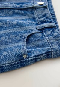 Sinine teksariidest kangas, millel on peen muster, nähtav tasku ja metallnupu detail, mis annab kangale struktuurse väljanägemise.