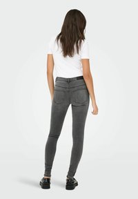 Harmaat kapeat farkut korkealla vyötäröllä, joissa on erottuva ompelu ja kaksi takataskua. Yhdistettynä yksinkertaiseen valkoiseen t-paitaan ja mustiin kenkiin.