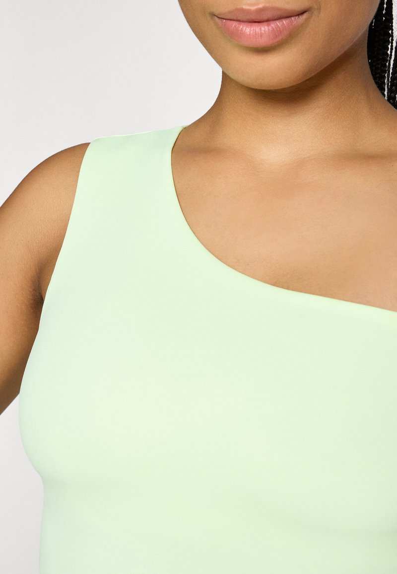 Top senza maniche verde chiaro con scollatura asimmetrica, texture liscia e design aderente, che mette in risalto la clavicola e la spalla.