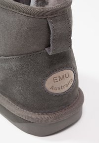 Graue Wildleder-Stiefelette mit runder Plakette mit der Aufschrift "EMU Australia". Strukturiertes Gewebe, weiche Fütterung und eine robuste Gummisohle.